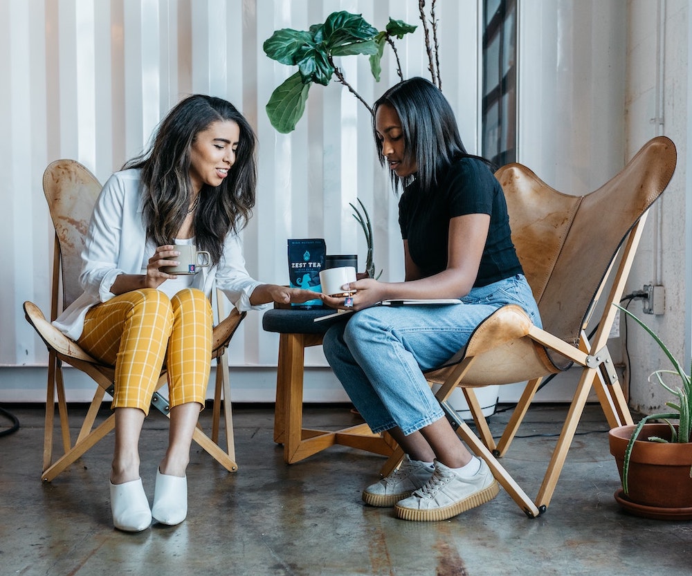 Two ladies sitting on a chair talking and smiling